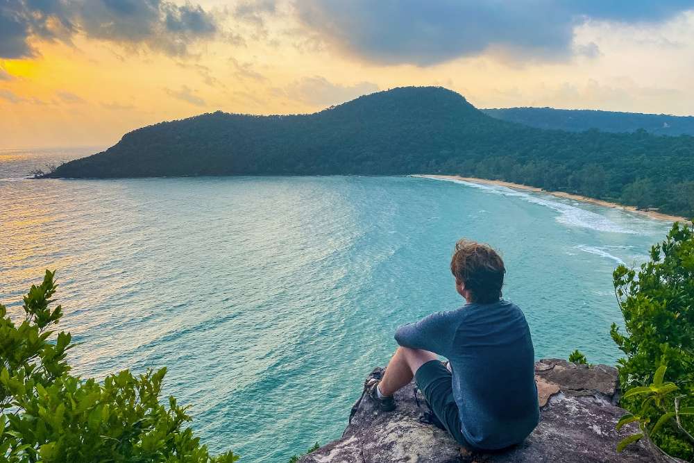 Touristes assis sur un rocher regardant le coucher de soleil sur la plage Lazy à Koh Rong